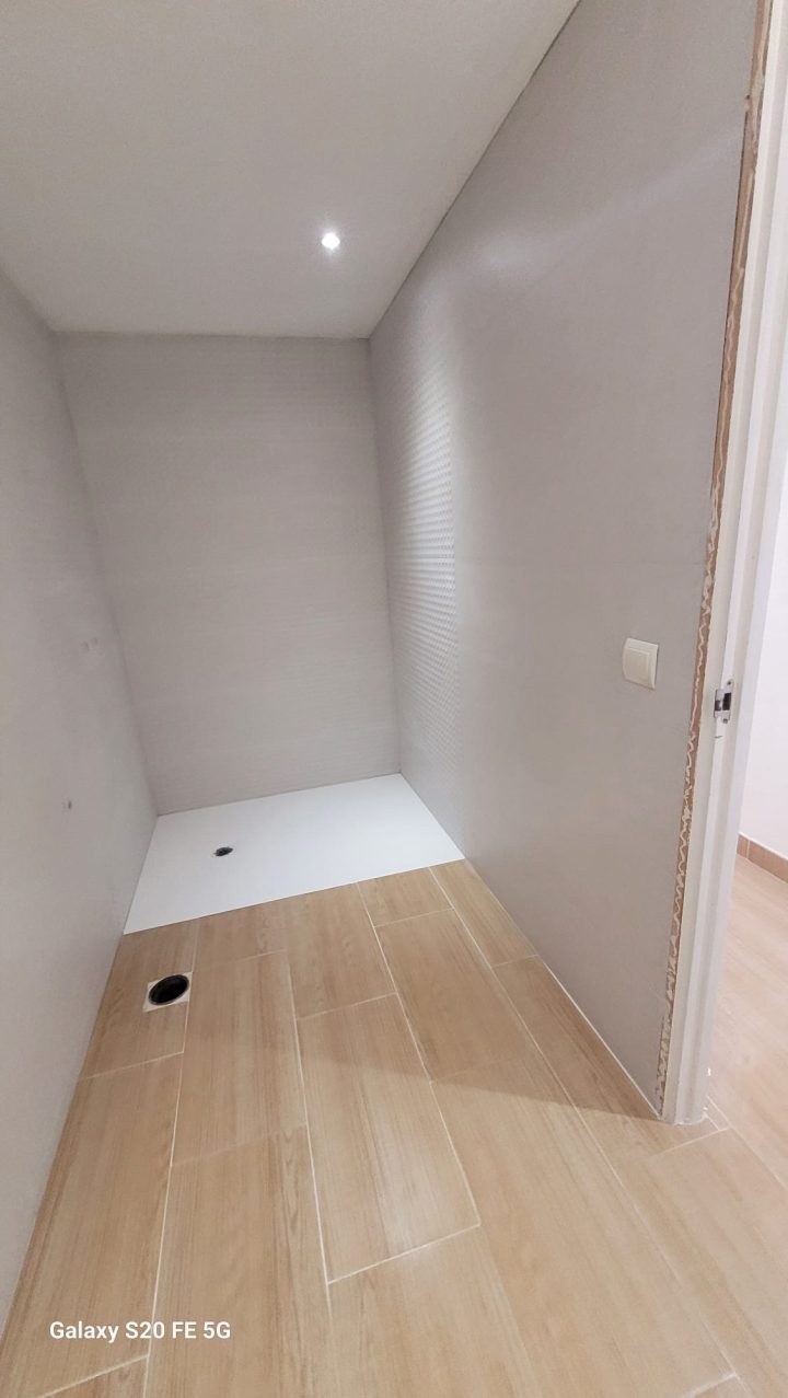 Baño reformado con plato de ducha blanco extraplano, paredes alicatadas en gran formato y suelo imitación madera