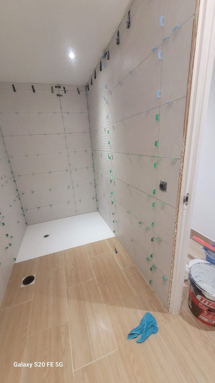 Baño en obra: alicatado de gran formato colocado con separadores de nivelación junto al plato de ducha blanco