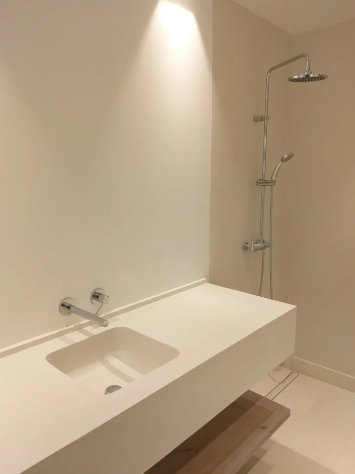 Baño reformado con encimera blanca suspendida, lavabo integrado y ducha con rociador, paredes en tonos crema