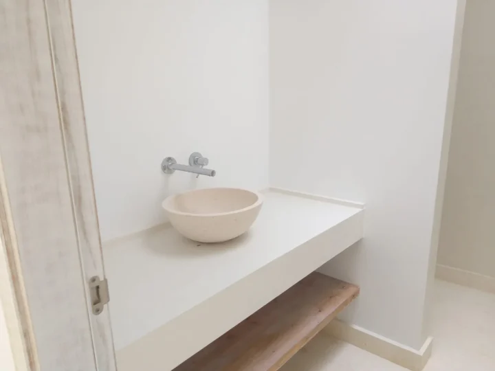 Lavabo de piedra sobre encimera blanca con grifo de pared y paredes lisas blancas