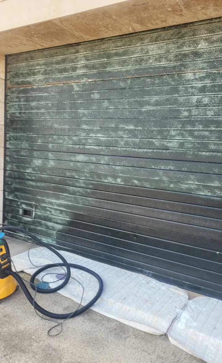 Lijado de una puerta de garaje con aspirador para retirar el polvo, antes de pintar