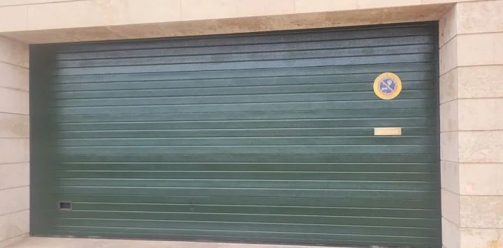 Puerta de garaje repintada en verde oscuro, vista frontal entre jambas de piedra