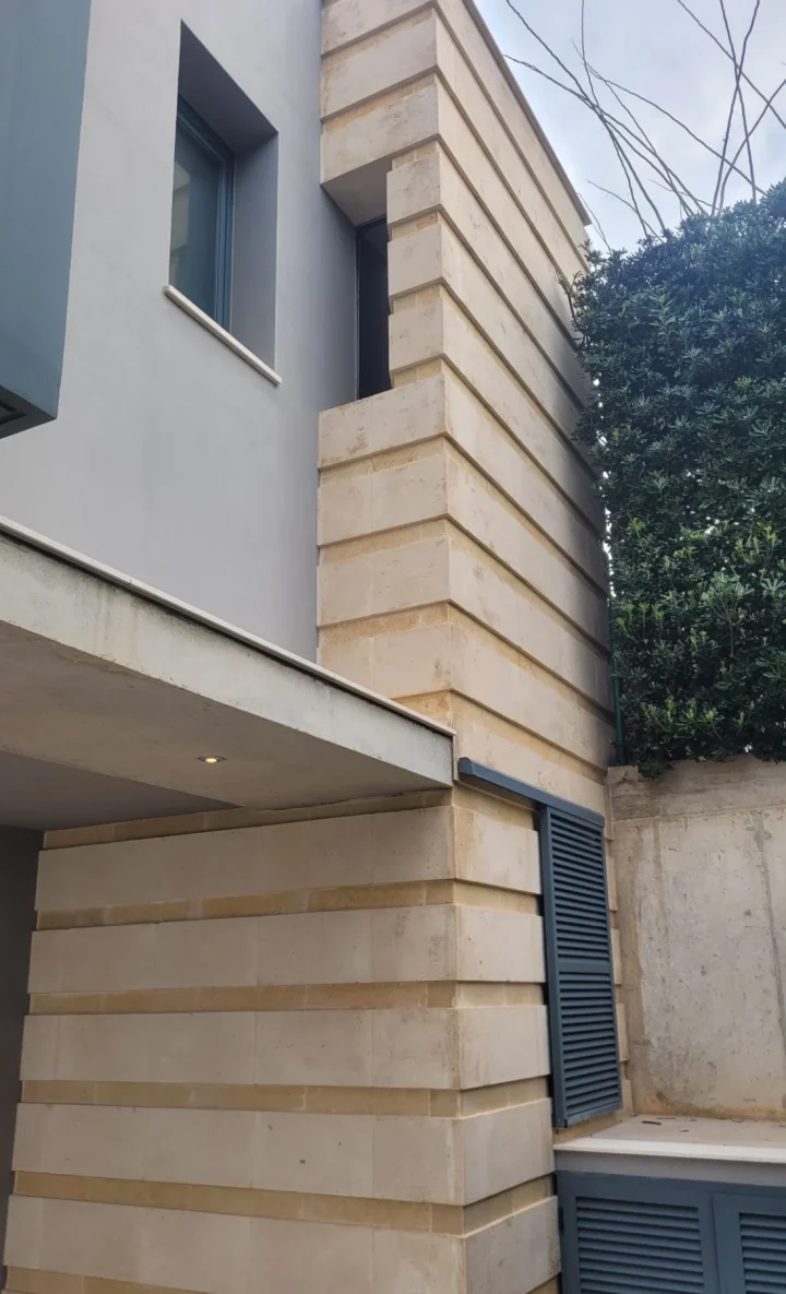 Fachada de piedra de marés en hileras junto a ventana y contraventanas azul grisáceo