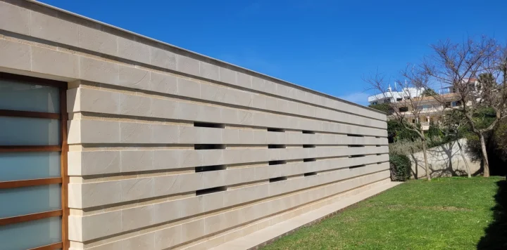 Muro largo de piedra de marés en un jardín, con hileras horizontales y ranuras de ventilación